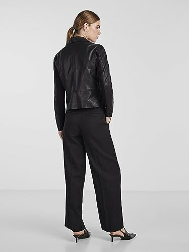 Mujer con chaqueta de cuero negra y pantalones oscuros.