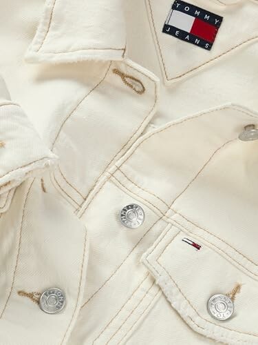 Chaqueta de mezclilla crema con botones plateados y etiqueta.