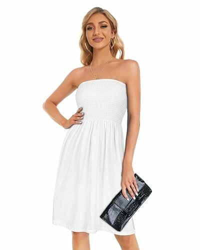 Mujer con vestido blanco sin tirantes sosteniendo un bolso negro.
