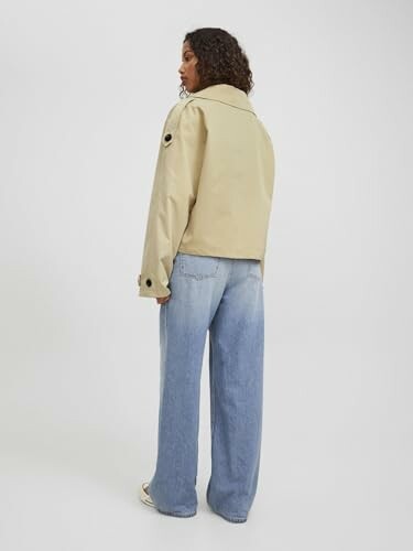 Mujer con chaqueta beige y jeans azules.