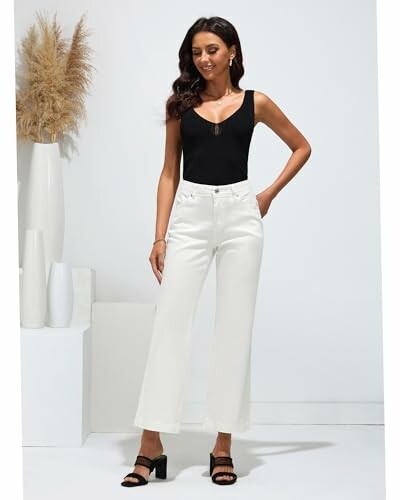 Mujer con top negro y pantalones blancos posando.